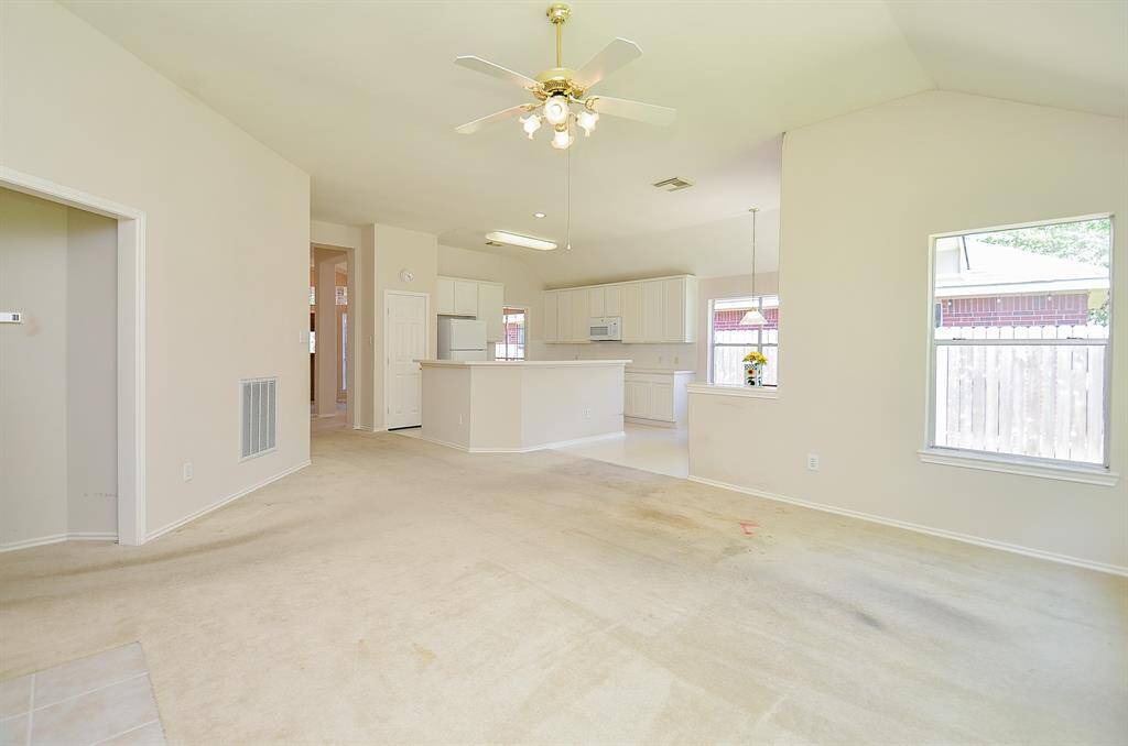 spacious open-plan living area with a plenty of natural light. The kitchen features white cabinetry and a central island, and the room has a neutral color palette, offering a versatile space for customization.