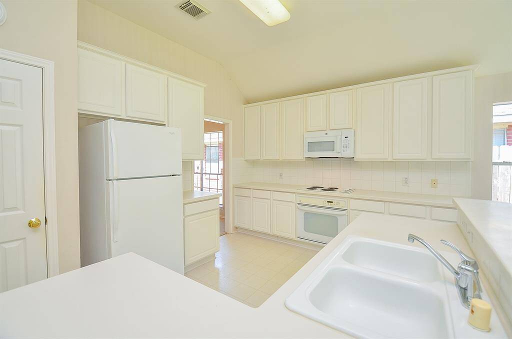 Bright, spacious kitchen with white cabinetry, ample countertop space, and white appliances. Features a double sink and plenty of natural light from the windows.