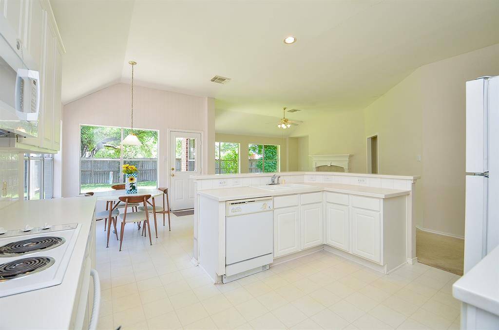 Bright, open kitchen with white cabinetry and appliances. Features a cozy dining area by a large window overlooking the backyard. Adjacent to the living space with a fireplace, creating a welcoming atmosphere.