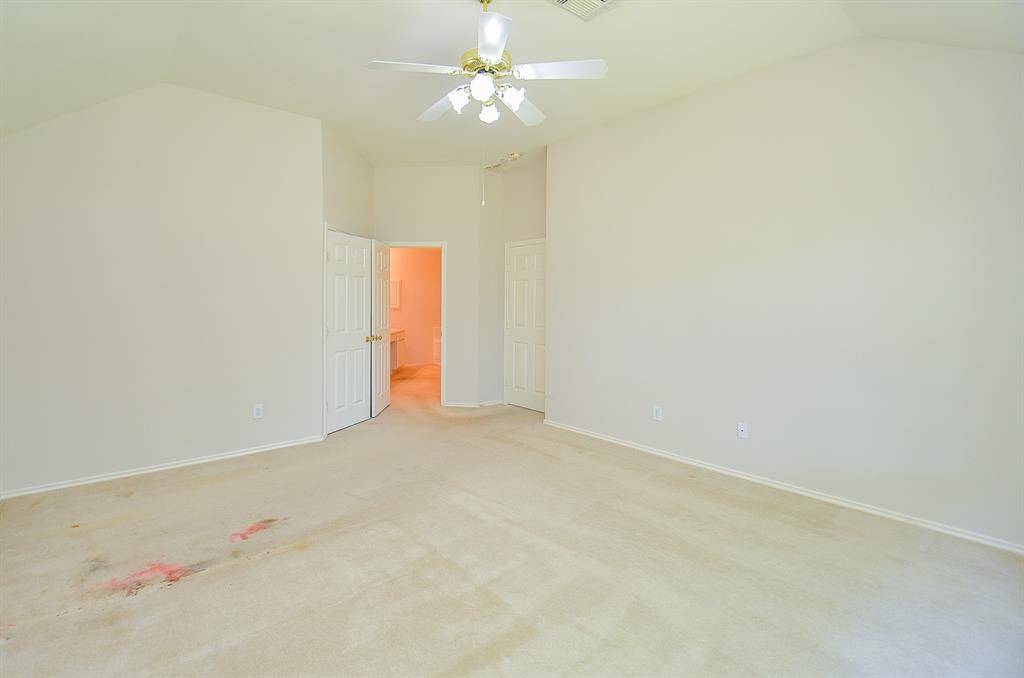 Spacious room with high ceilings and neutral walls, featuring a ceiling fan. It has double doors leading to an adjacent area and another door to a bathroom. The carpet just needs replacing.