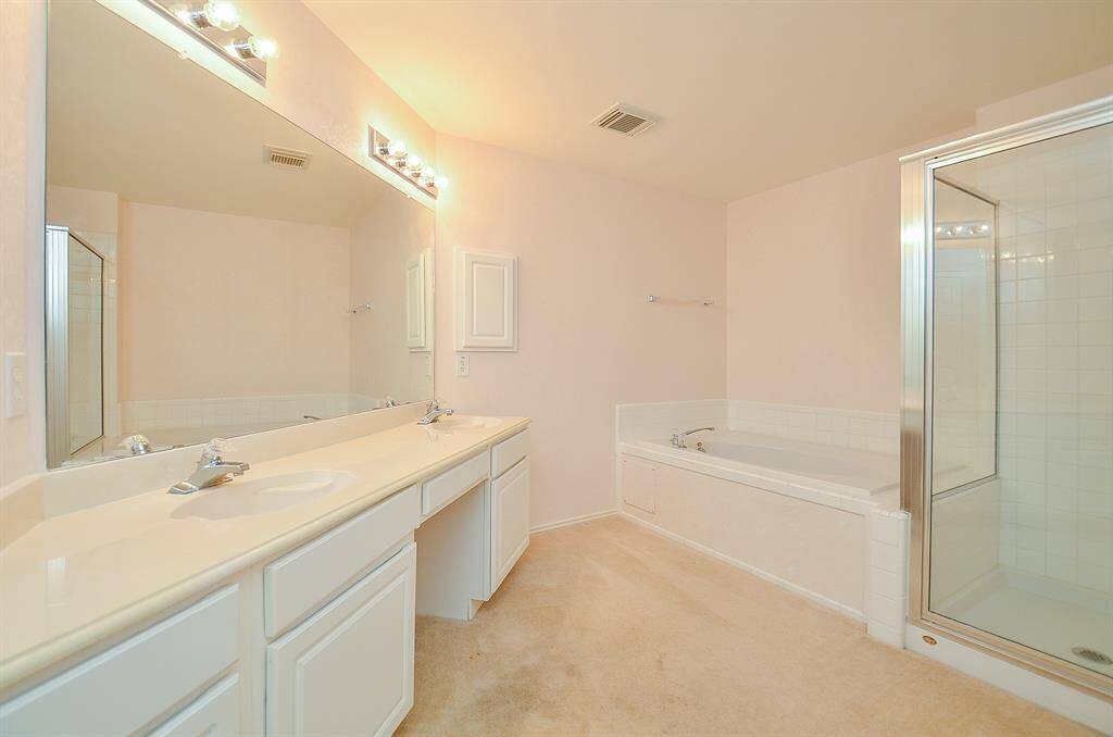 This spacious bathroom features a large double vanity with ample storage, a corner bathtub, and a separate glass-enclosed shower, all in a bright, neutral color scheme.