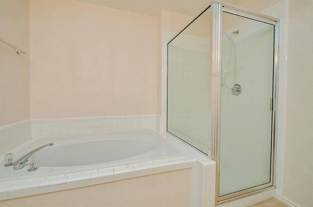 This bathroom features a spacious bathtub with tile surround and an adjacent glass-enclosed shower, offering a clean and modern design.