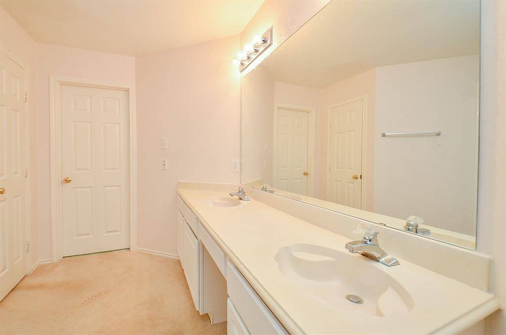 Bright bathroom with a large mirror and dual sinks, offering ample counter space. The room features neutral tones and clean lines, creating a spacious and inviting atmosphere.