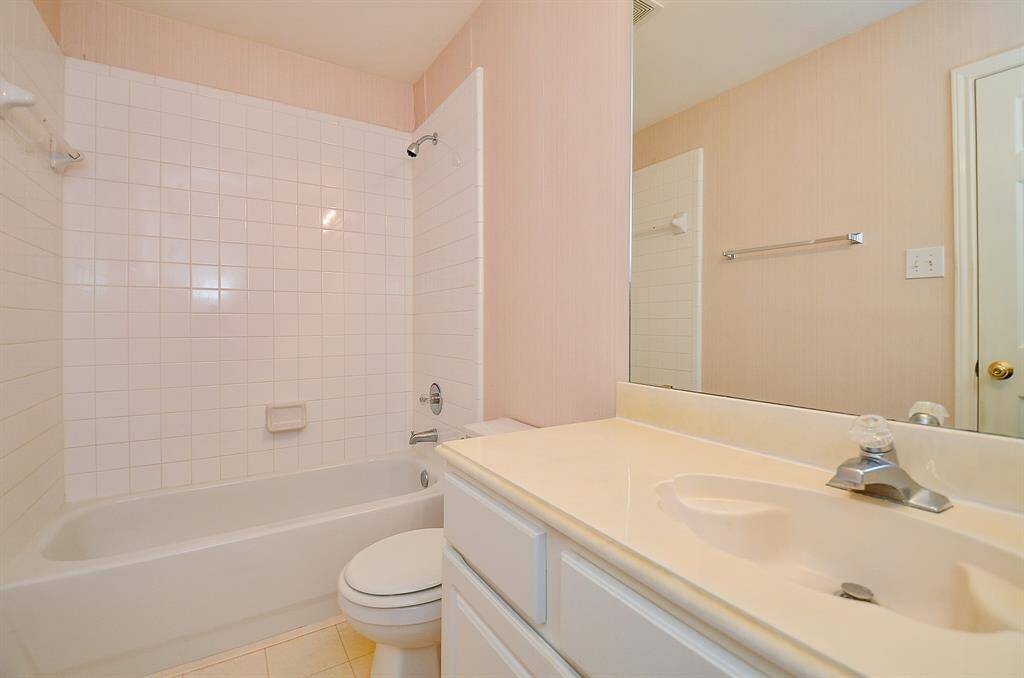 This bathroom features a clean, simple design with a white tile bathtub and shower combination. It includes a single sink vanity with ample counter space, a large mirror, and neutral wall tones, creating a bright and inviting space.