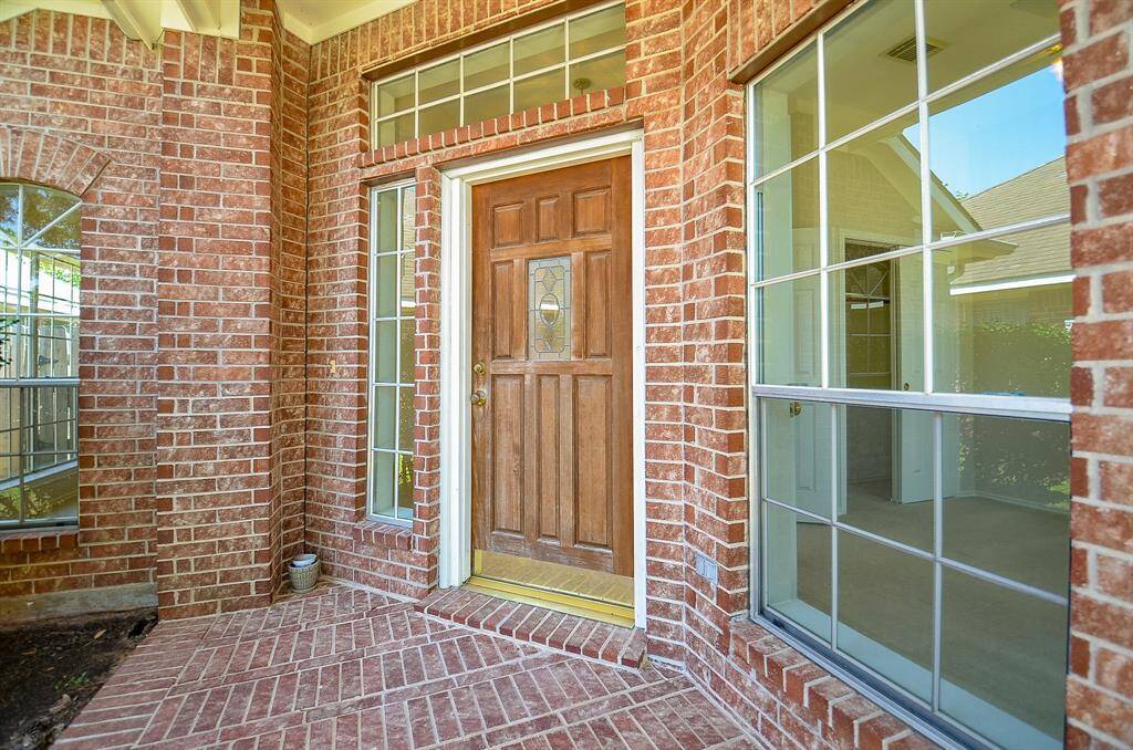 Charming brick entryway with a wooden front door and large windows, offering a welcoming and bright atmosphere.