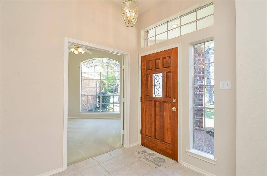 Bright entryway with a wooden front door featuring decorative glass. Neutral tile flooring complements the airy feel.