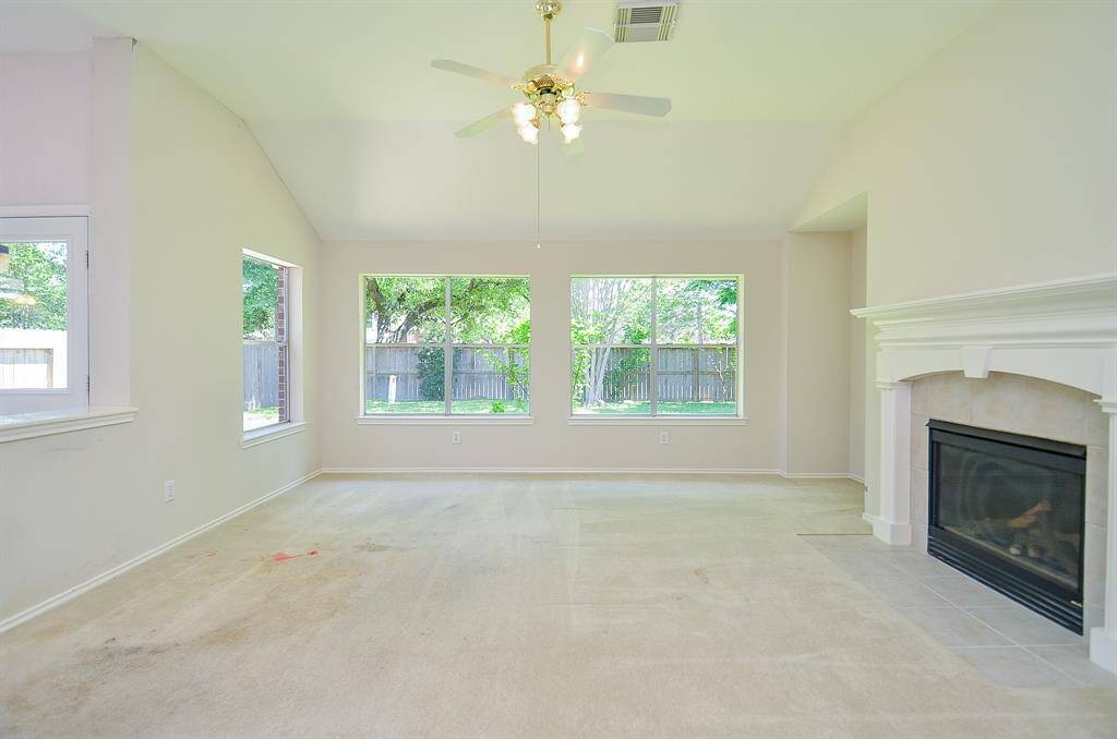 Bright living room with large windows offering lush views, a cozy fireplace, and a ceiling fan. Neutral walls provide a blank canvas for personalization.