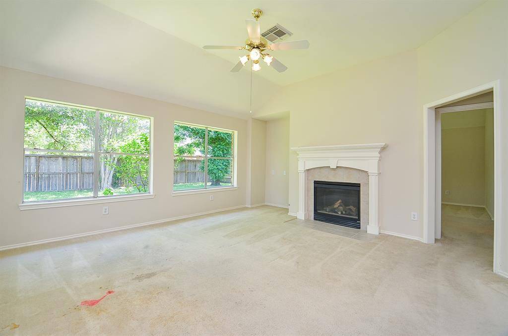 This bright living room features large windows with garden views, a ceiling fan, and a cozy fireplace.