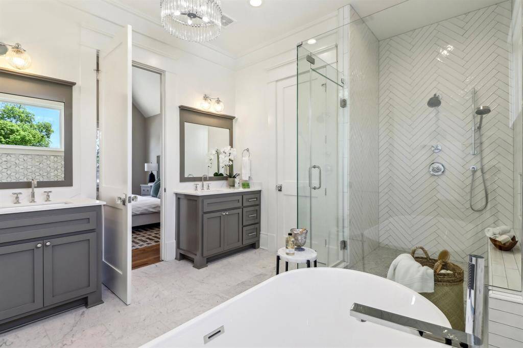 The primary bath is a dream-space. Every design element is on point, adding visual interest without overdoing it. The dual vanities are painted in contrast to the sunbathed hue of the walls, and they work in synergy with the coloring in the marble flooring, grout, and wall of tile (noticable in the mirror reflection, but pictured henceforth in another photo). You will appreciate their own vanity spaces being seperated.