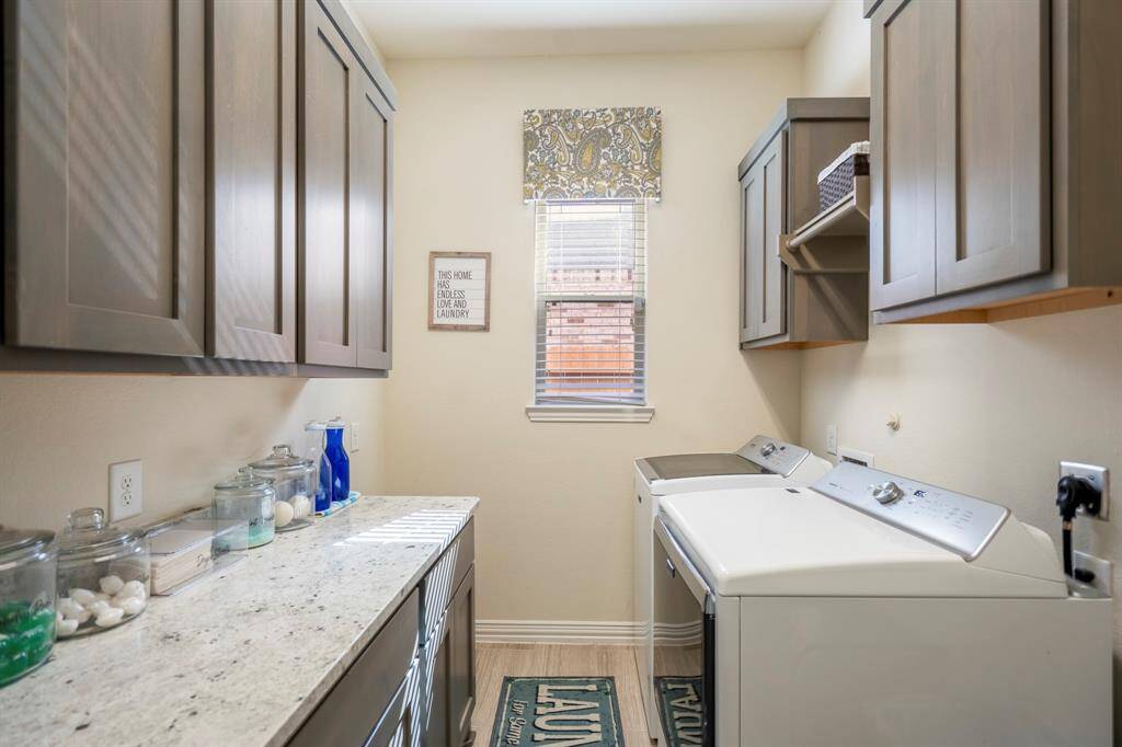 A large laundry room offers lots of storage with upper and lower cabinetry, a large folding granite countertop, and window for natural light.
