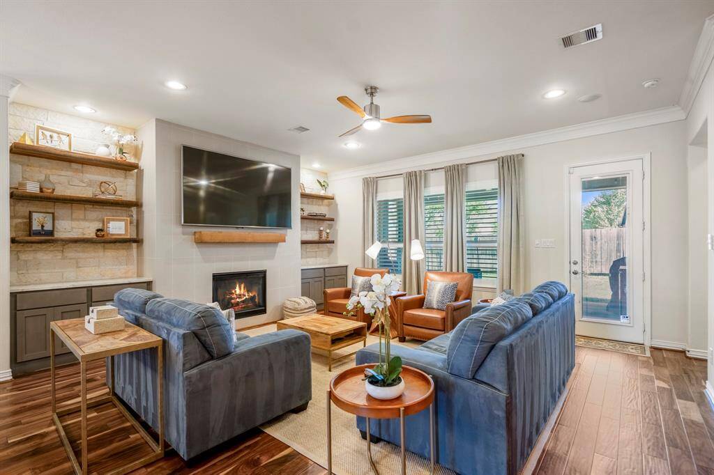 The den has a tiled wall with gas log fireplace, wood mantel and is flanked by wooden shelves and cabinetry to additional storage.