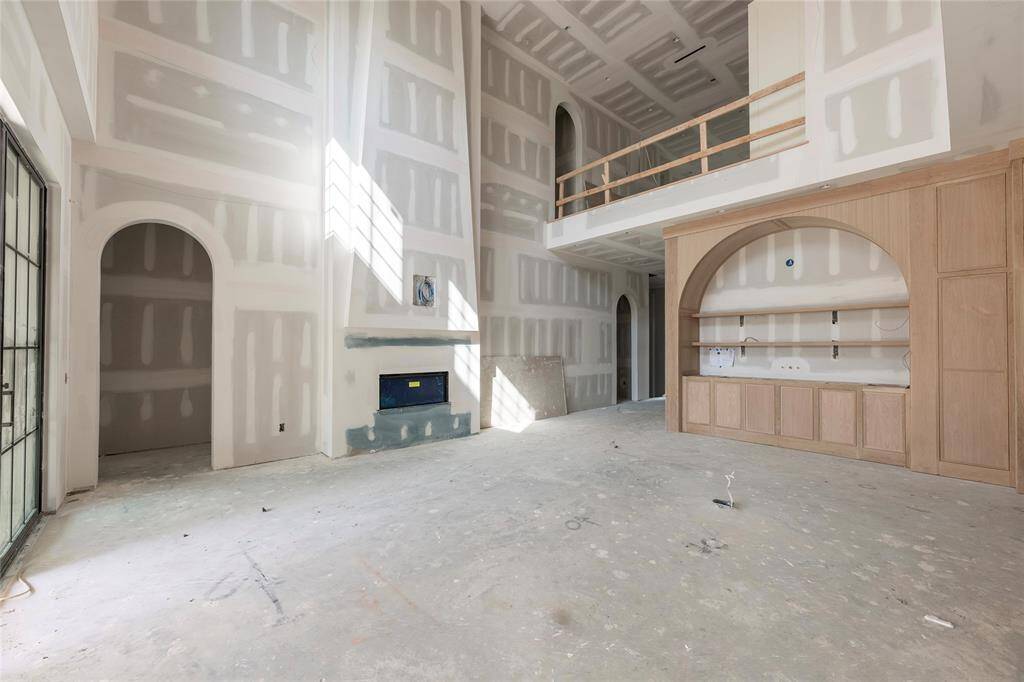This image showcases the impressive space of the open-concept living area, featuring high ceilings as the centerpiece to the living area is a two story fireplace. The secondary living area also overlooks the primary great room which will have custom wrought iron ballusters and wood hand rail.