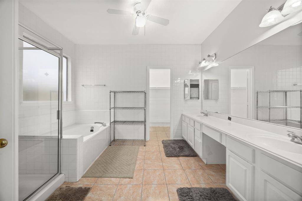 Spacious primary bathroom featuring dual vanities, a soaking tub, separate glass-enclosed shower, and plenty of storage - your personal spa escape at home.