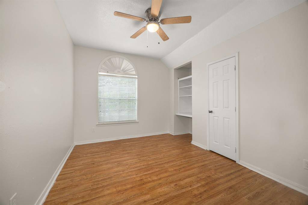 Cozy secondary bedroom with built-in shelving, wood-style flooring, and a charming arched window that brings in natural light.