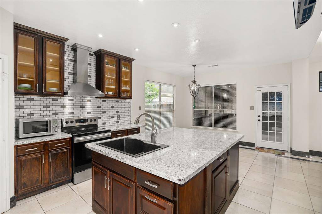 Bright and open kitchen space featuring granite countertops, a deep farmhouse sink, stainless steel range hood, and a cozy breakfast area with backyard views - perfect for everyday living or hosting guests.