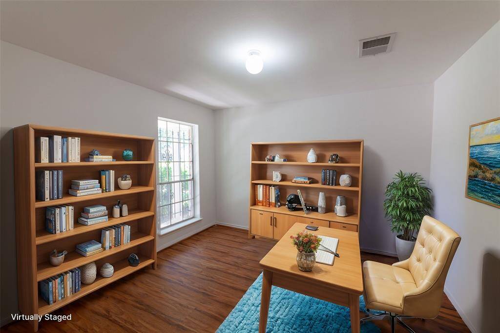 A bright, virtually staged home office in the flex room with wood flooring and a large window. It features two bookshelves, a desk with a comfortable chair, and decorative elements that create a cozy and functional workspace.