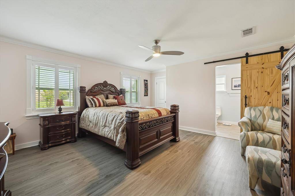 Spacious primary suite with dual windows, luxury vinyl plank flooring, and a charming barn door to the en-suite bath.