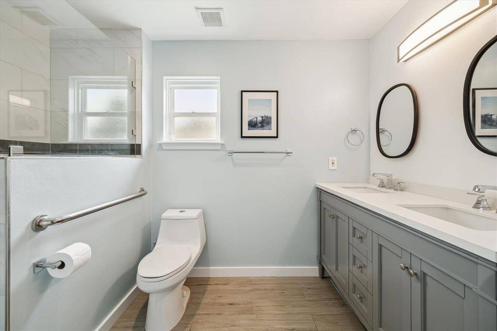 The reimagined primary bath features a dual vanity with sleek finishes, framed mirrors, and stylish lighting.