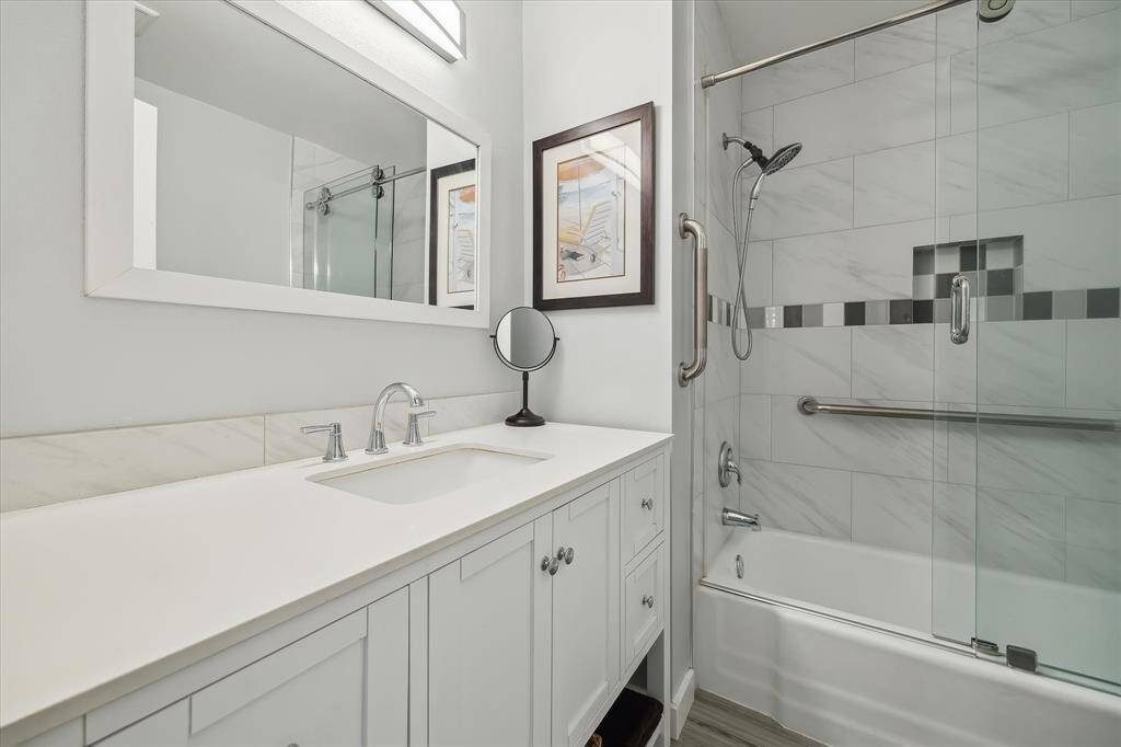 Remodeled secondary bath (2019) with quartz countertops, updated vanity, tiled tub/shower surround, glass shower doors, and clean contemporary style.