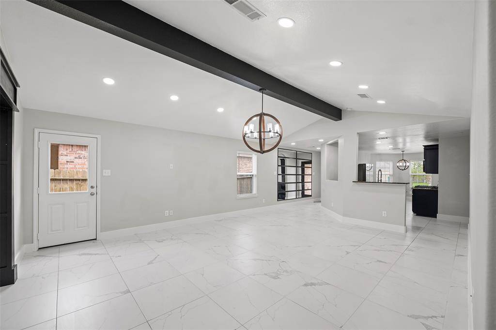 This photo showcases a modern, open-concept living area with sleek white tile flooring, recessed lighting, and a contemporary chandelier. The space seamlessly connects to the kitchen, featuring a serving counter, and offers plenty of natural light through large windows.