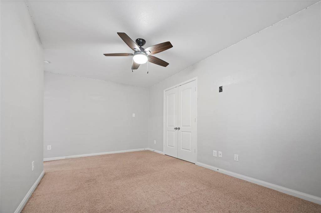 This photo showcases a clean, carpeted room with light gray walls, a ceiling fan with a light fixture, and double doors, offering a simple and functional space.
