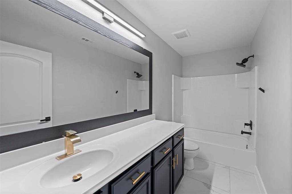 This bathroom features a modern design with a large mirror, sleek vanity with gold fixtures, and a combination shower/tub. The space is bright with neutral tones and stylish accents.