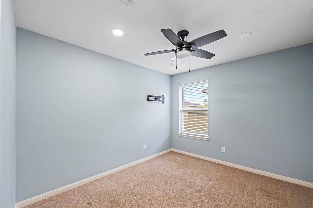 This cozy room features soft blue walls, a ceiling fan with lights, and a window for natural light. The space is carpeted and has a wall bracket for mounting a TV. Perfect for a bedroom or office.