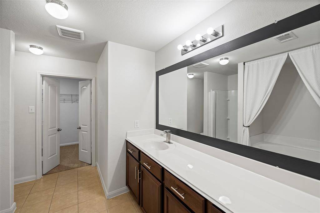 This bathroom features a spacious double vanity with dark wood cabinets, a large mirror, and bright lighting. It includes a bathtub with a curtain and a separate shower, offering a modern and clean design.