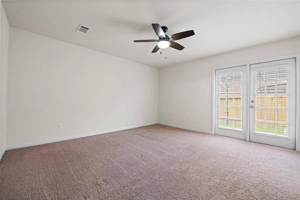 Spacious, carpeted room with neutral walls and a ceiling fan. Features double French doors leading to a fenced backyard, allowing natural light to brighten the space.