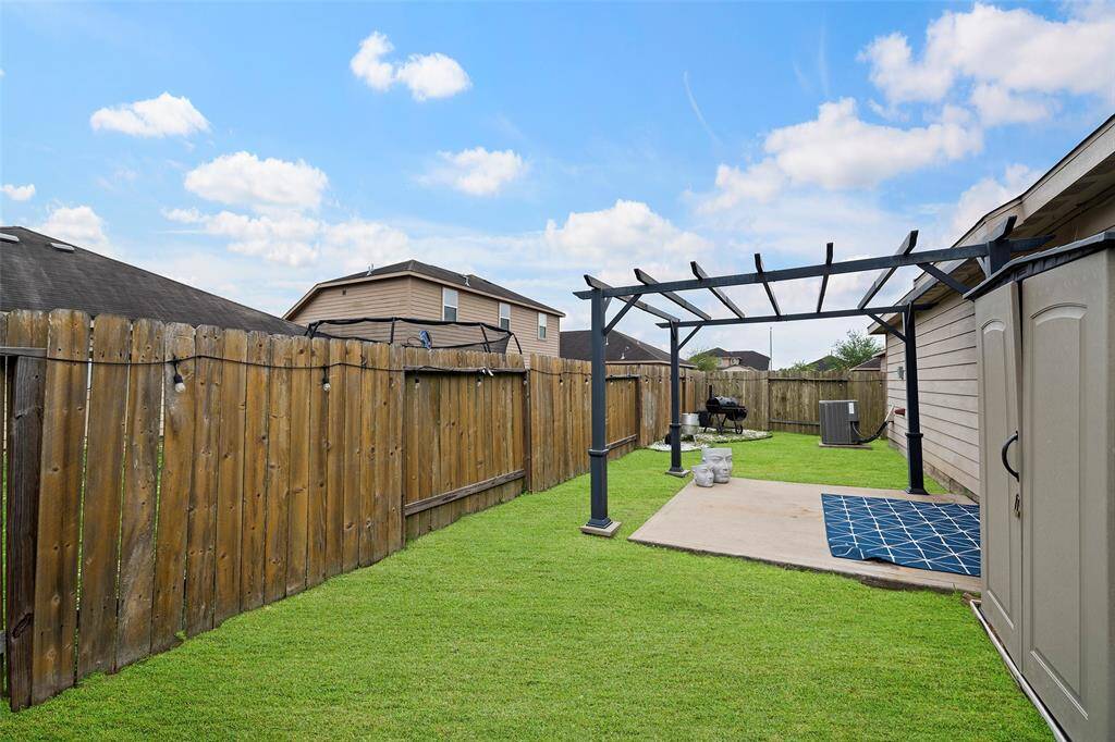 Charming backyard with a pergola, perfect for outdoor entertaining. Features a small patio area, lush grass, and a wooden fence for privacy.