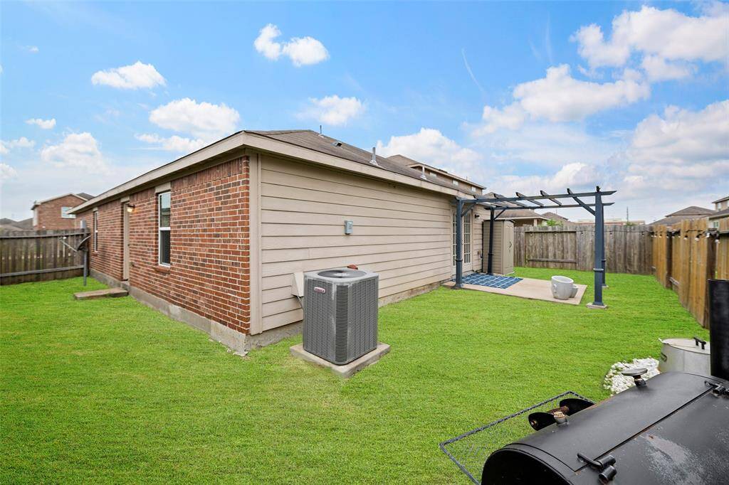 This photo shows a spacious backyard with a well-maintained lawn, a brick and siding exterior, a pergola-covered patio area, and a fenced perimeter for privacy. Ideal for outdoor activities and relaxation.