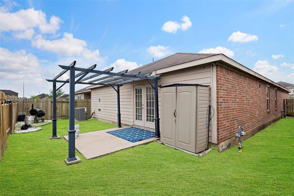 This backyard features a well-maintained lawn with a wooden pergola over a concrete patio, perfect for outdoor relaxation. A storage shed is conveniently placed beside the house, which has a brick exterior. A fenced boundary provides privacy and security.