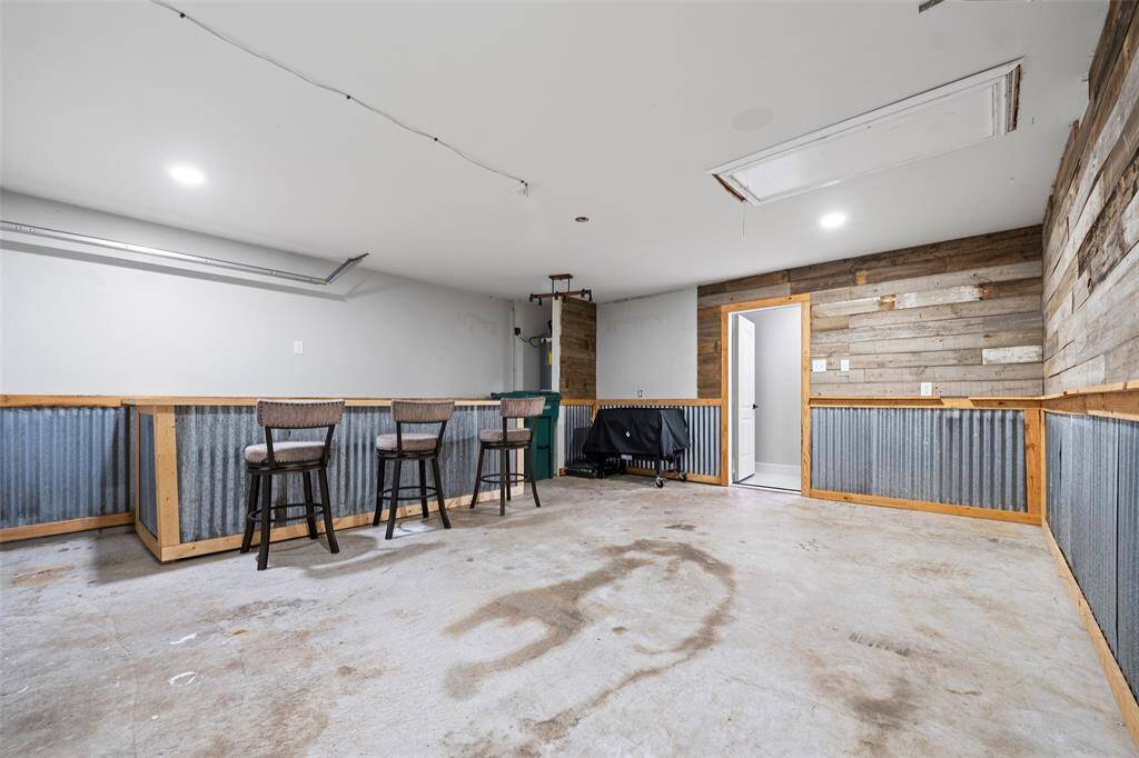 This spacious room features a rustic design with corrugated metal wainscoting and wood paneling. It includes a bar area with seating and offers a blank canvas for customization. Ideal for a game room or workshop.