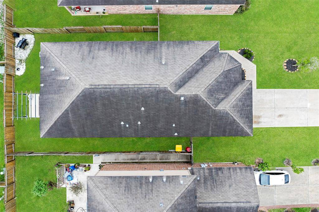 This aerial view showcases a well-maintained home with a large roof, spacious driveway, and a neatly landscaped yard. The property is fenced, offering privacy and a defined outdoor space.