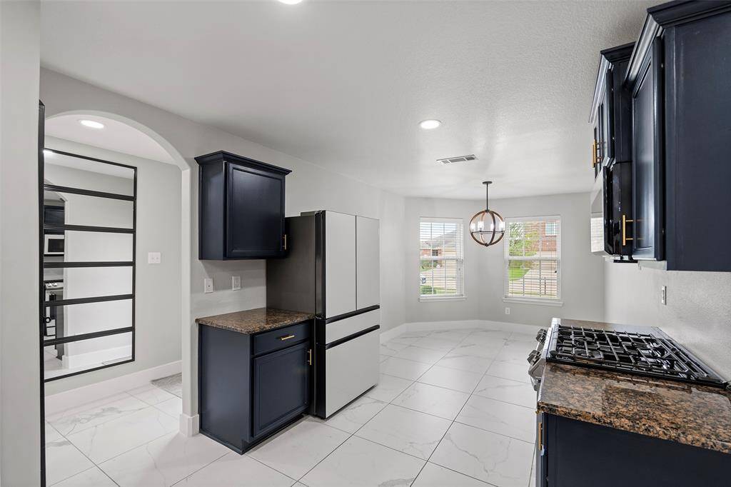 Modern kitchen with sleek dark cabinets, granite countertops, and white tile flooring. Includes a gas stove, contemporary light fixture, and a bright breakfast nook with large windows.