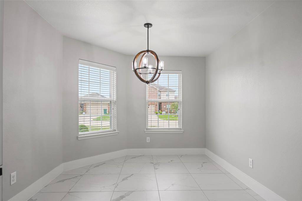 Bright dining area with large windows, modern light fixture, and sleek tile flooring, offering a clean and inviting atmosphere.