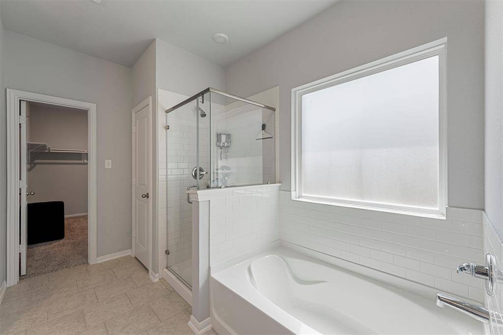 Spa-like primary bathroom featuring a soaking tub, separate glass-enclosed shower, and a large walk-in closet.