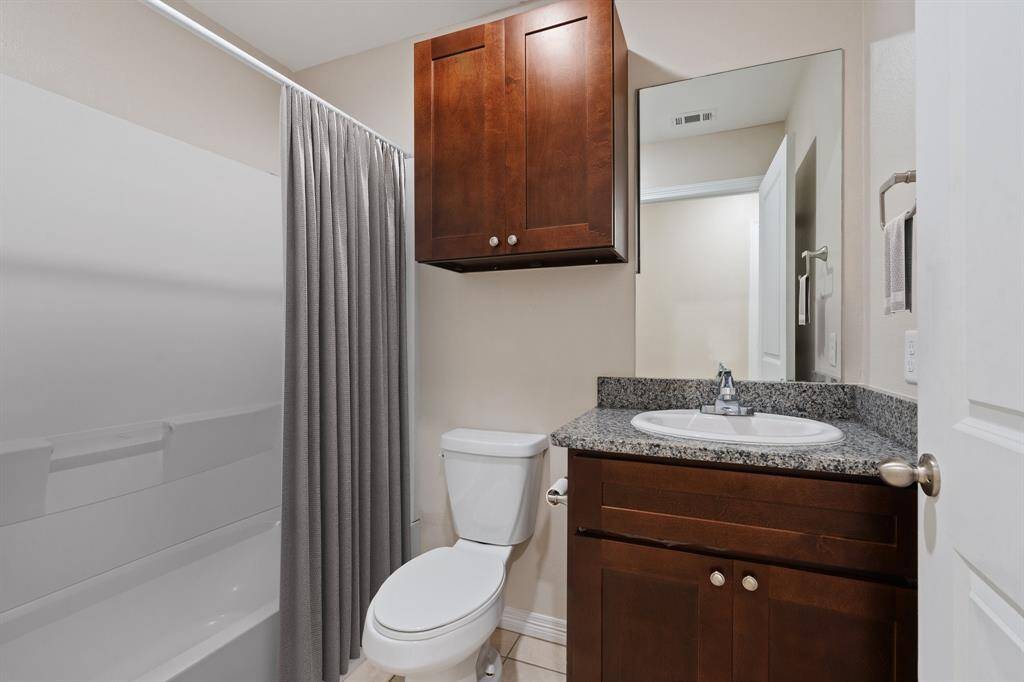 This is auspicious secondary bathroom featuring a tub with a shower, a wood-finished vanity with a granite countertop, an undermount sink, and a mirrored medicine cabinet above. The space is well-lit and a functional design.