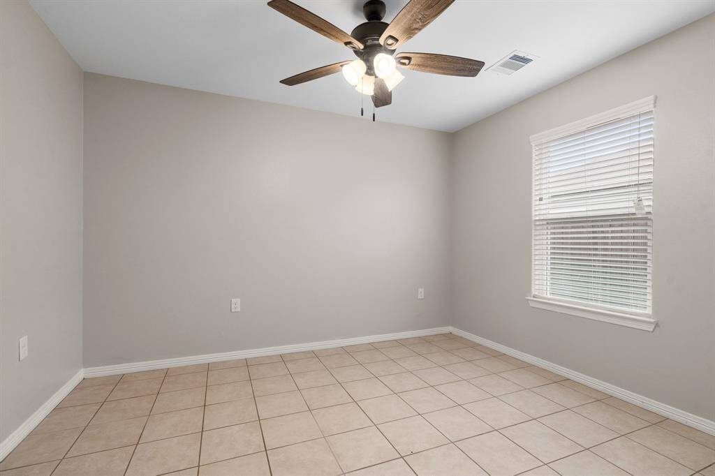 This is an additional bedroom featuring neutral walls, tile flooring, a ceiling fan with lighting, and a window with horizontal blinds, allowing for natural light.
