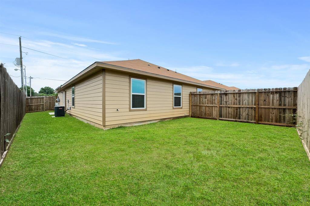 This photo shows a well-maintained backyard with a spacious, back yard and a privacy fence, alongside a single-story house with beige siding and windows for natural light.