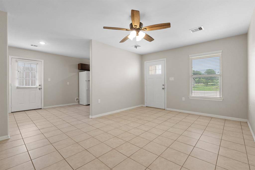 This is a spacious, well-lit room with neutral walls and tiled flooring. It features a ceiling fan and a window offering natural light.
