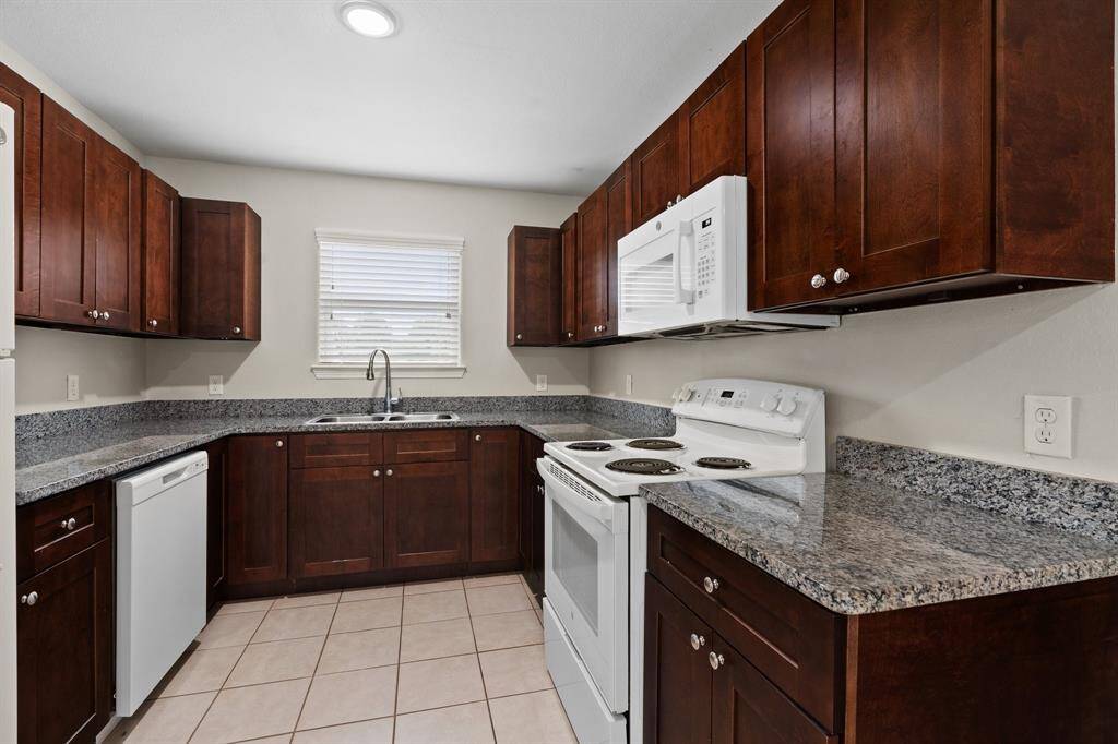 This is a well-maintained kitchen featuring rich, dark wood cabinetry, granite countertops, and includes modern appliances such as a dishwasher, range, and over-the-range microwave. The space is complemented by a tiled floor and offers ample storage and prep space.