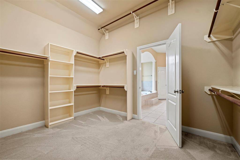 A spacious walk-in closet features ample shelving and hanging space. The neutral tones and carpet flooring create a warm and functional storage area.