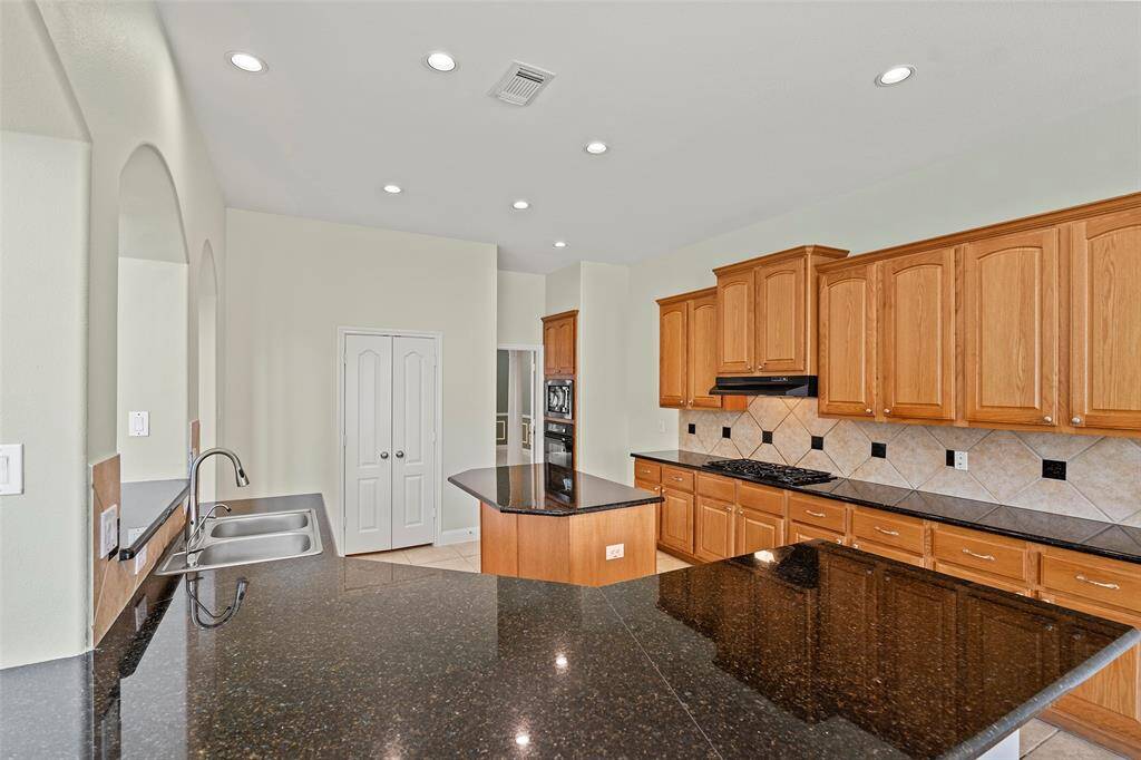 Spacious kitchen featuring granite countertops, ample wooden cabinetry, a central island, and a walk-in pantry. A modern, well-lit space with tiled backsplash.
