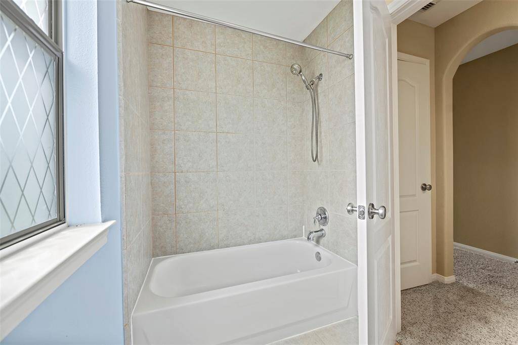 A clean, 3rd bathroom with a tiled bathtub and shower combination. There's a window with patterned glass for privacy and natural light.