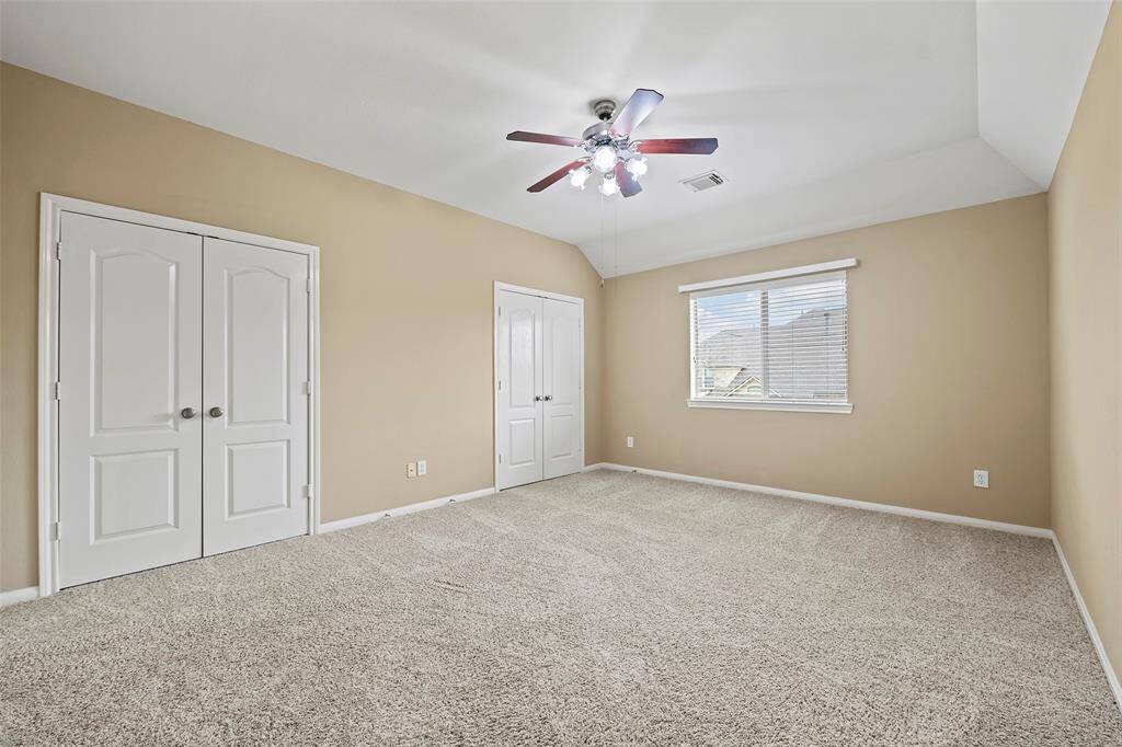 This spacious bedroom features a ceiling fan with lights, a large window providing natural light, and two closets with double doors for ample storage.