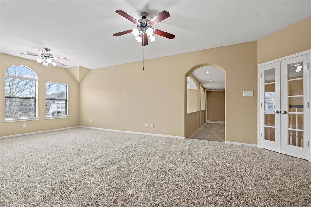 Expansive second-floor game room with natural light, elegant finishes, and French doors opening to a balcony with entry views.