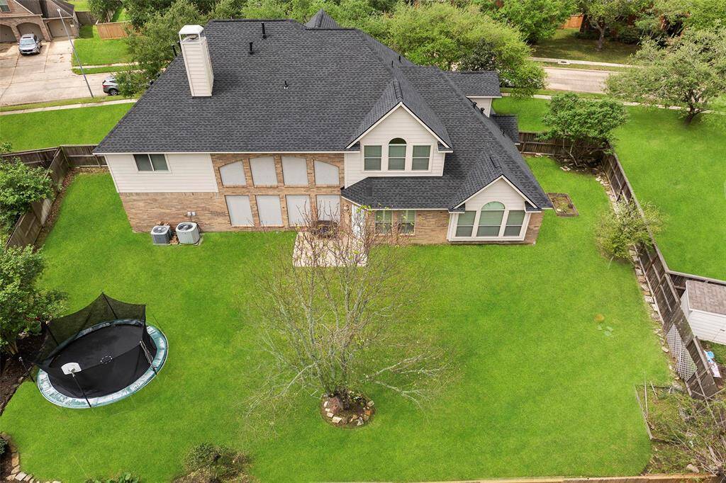 An aerial photo showcasing a spacious two-story home a mix of brick and siding exterior. The large backyard features a trampoline, mature trees, and is enclosed by a wooden fence, offering plenty of outdoor space.