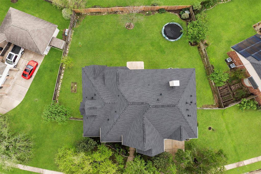 Experience a family-friendly oasis with this aerial view highlighting a spacious backyard, complete with a lush lawn and trampoline, all enclosed by a secure fence. The home boasts a brand-new roof (2024), offering both outdoor enjoyment and privacy.