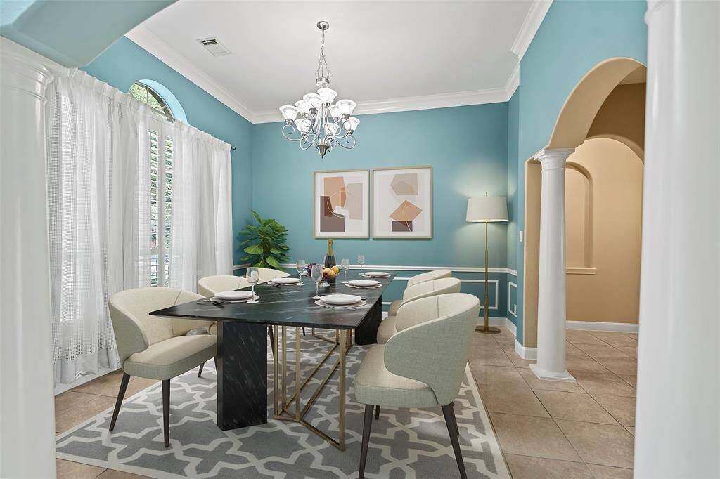 Elegant dining room with soft teal walls, crown molding, and a stylish chandelier. Features large windows with plantation shutters and sheer curtains for natural light. Virtually staged!!